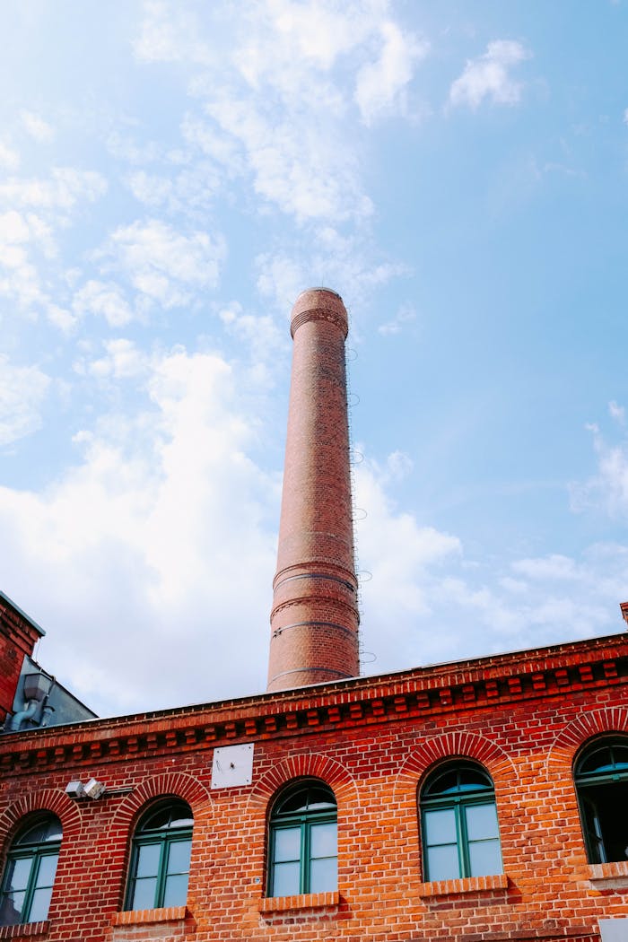 A striking view of an industrial building with a tall brick smokestack reaching into a vibrant blue sky.